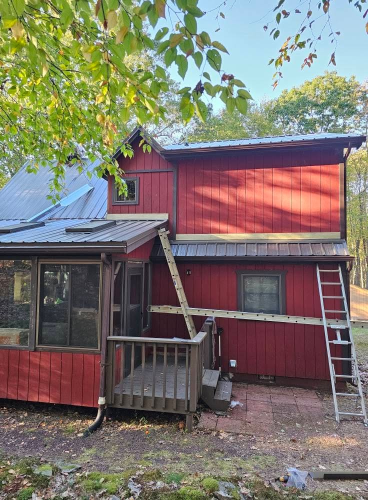 Wallenpaupack Roofers crew ladder set against a red lake house during a metal roof installation